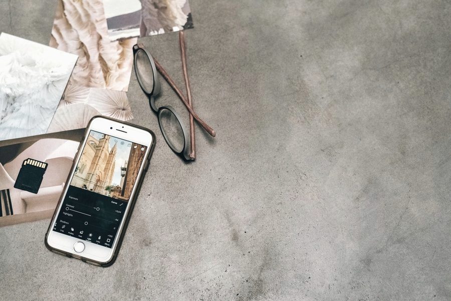 Smartphone mit geöffneter Foto-App, Brille und Abzüge auf einer Betonfläche