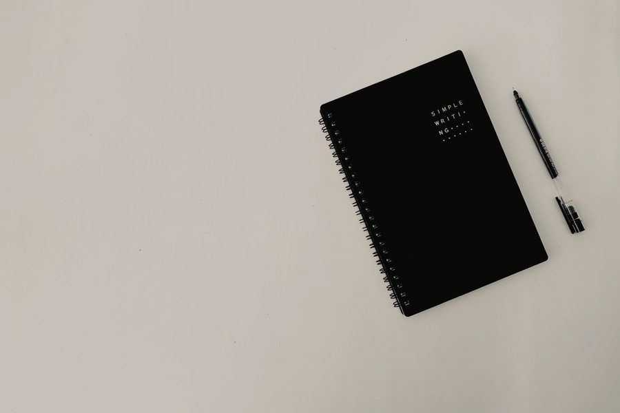 Schwarzes Notizbuch mit Stift auf einer hellen, ruhigen Fläche