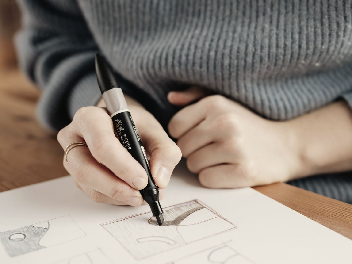 Hand zeichnet mit einem schwarzen Marker eine Layout-Skizze auf Papier, an einem hellen Holztisch